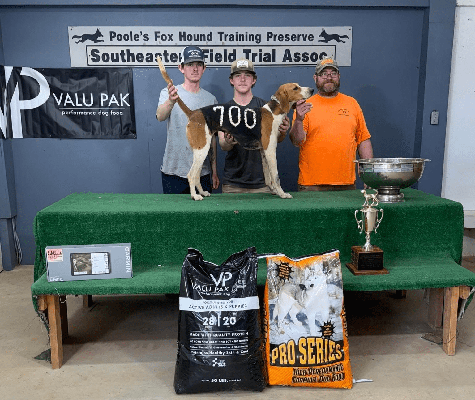 Three men with a dog and trophies.