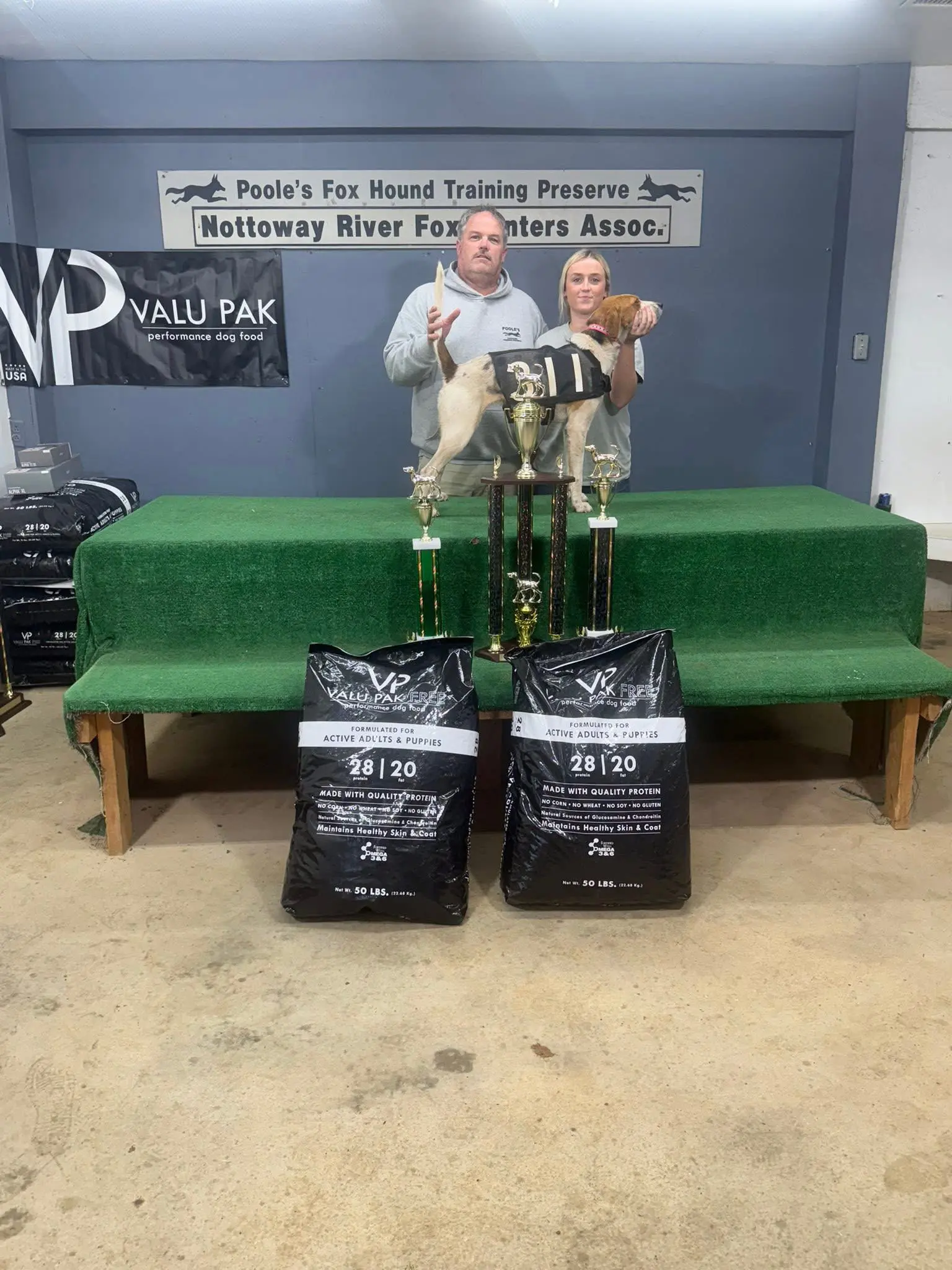 Two people with trophies and dog.