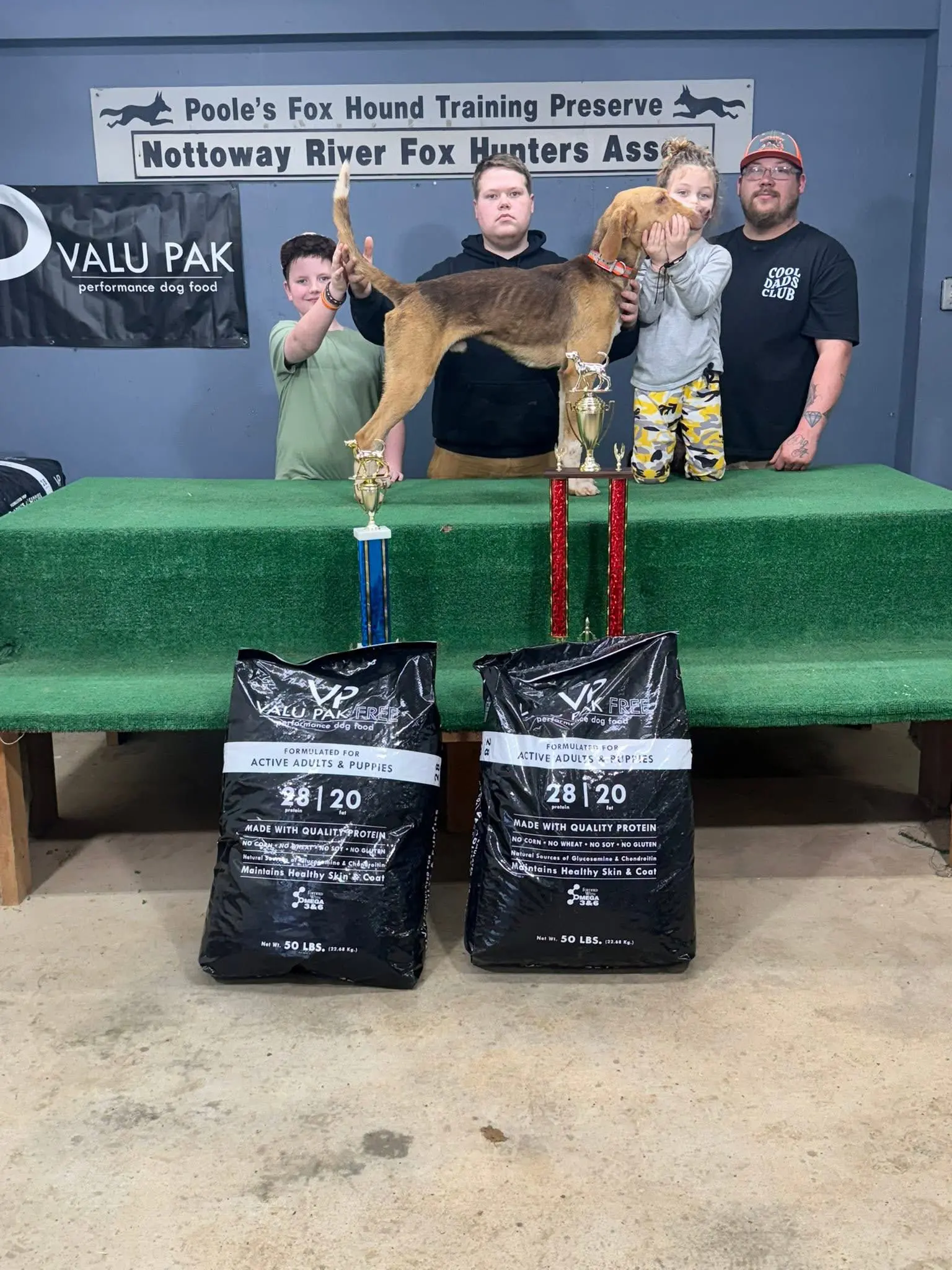 People with dog and trophies on table.