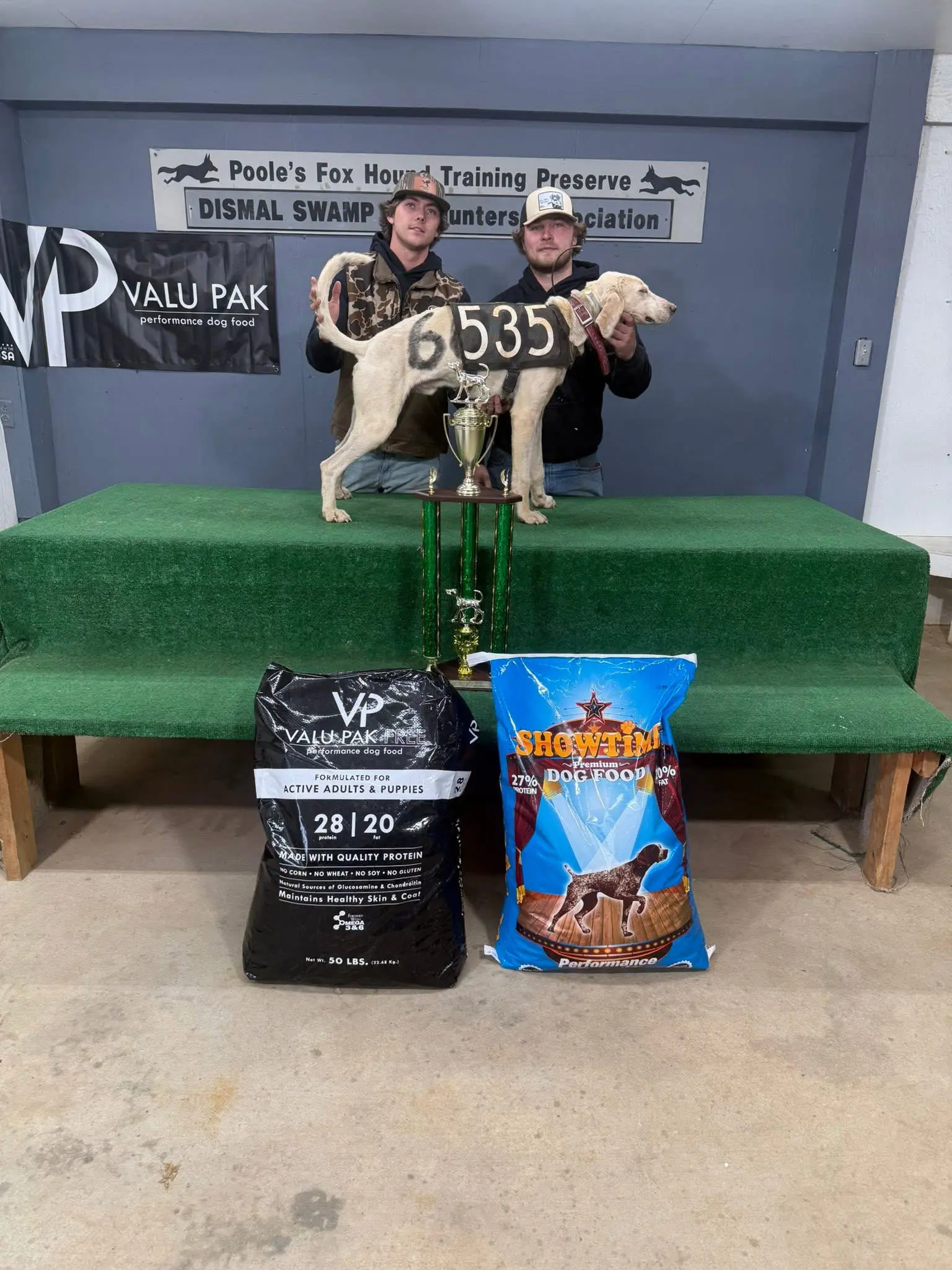Two men with award-winning dog and trophies.