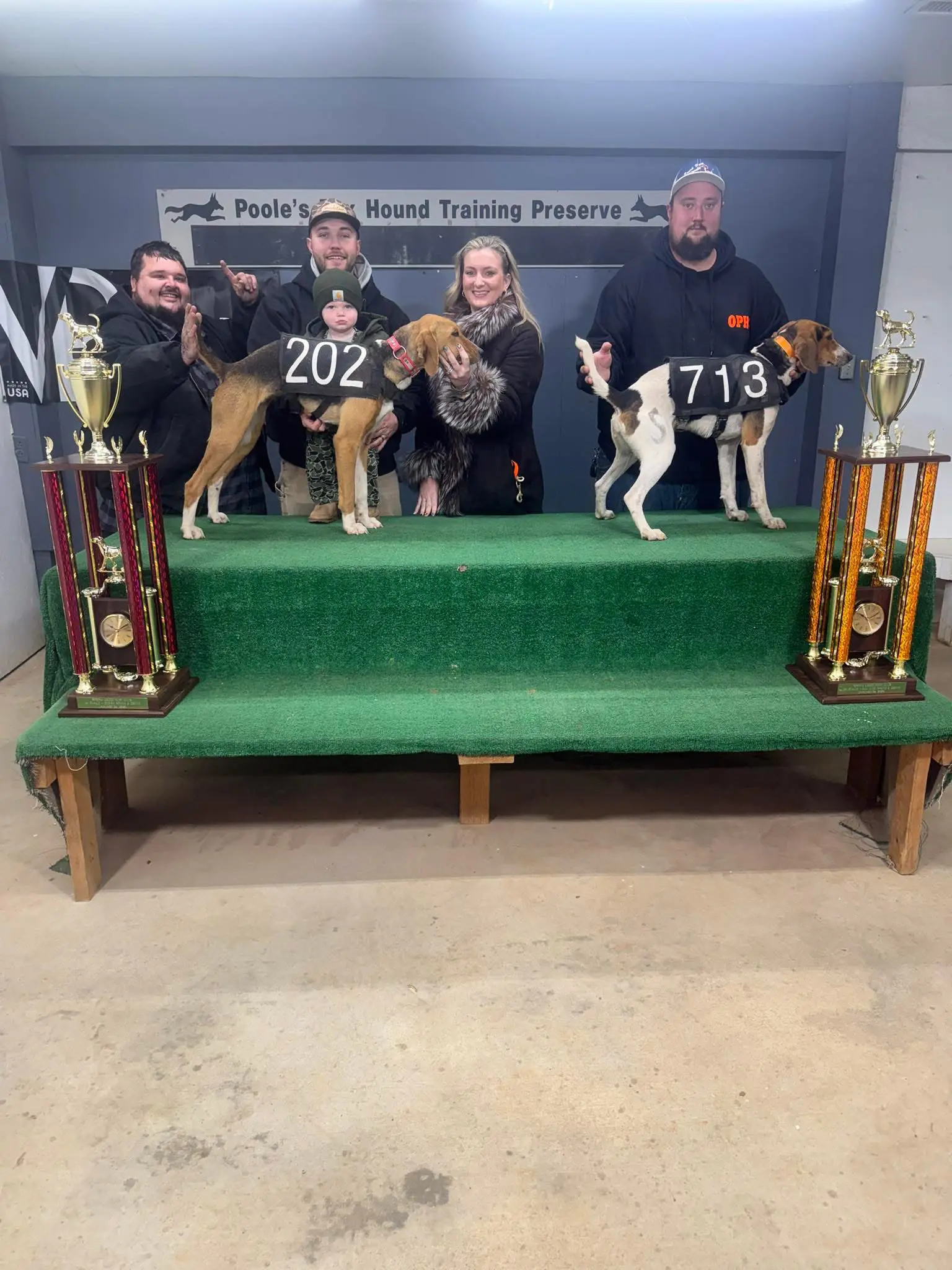 Dogs and owners with trophies on stage.