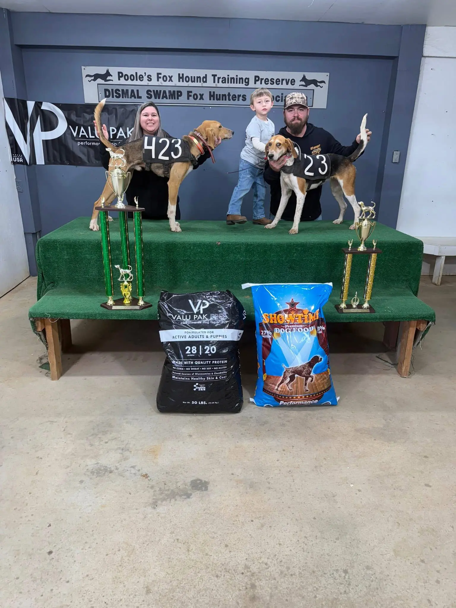 Two dogs on stage with trophies.