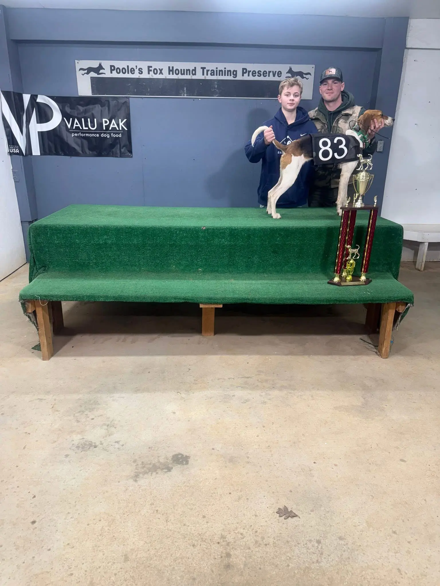 Two people with a dog and trophy.