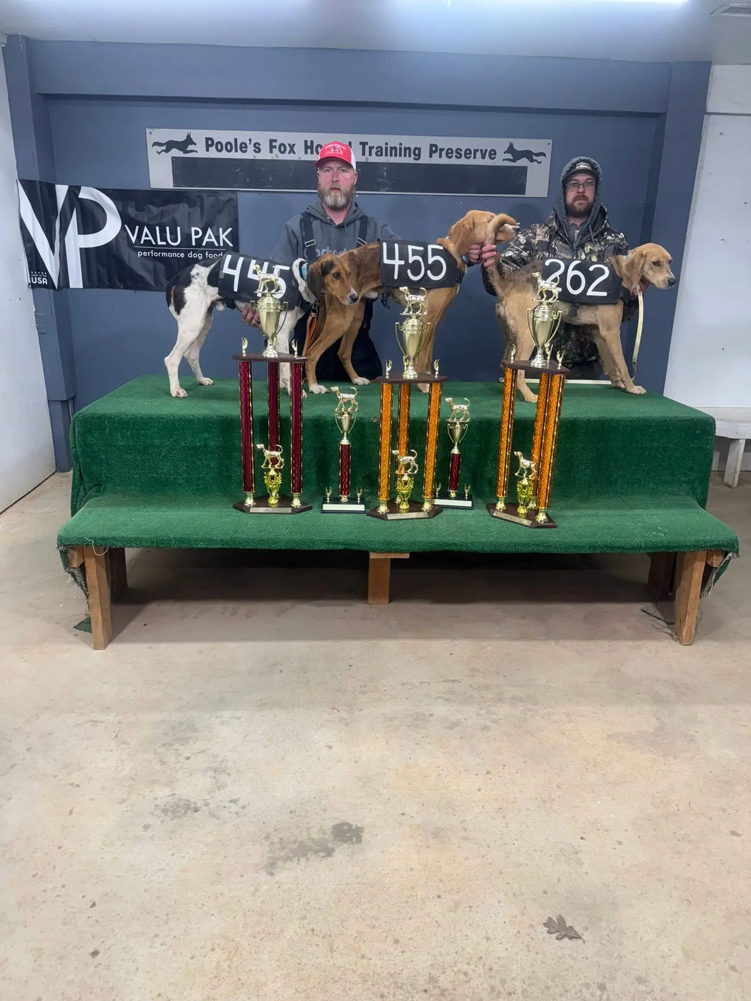 Two men with dogs and trophies on stage.