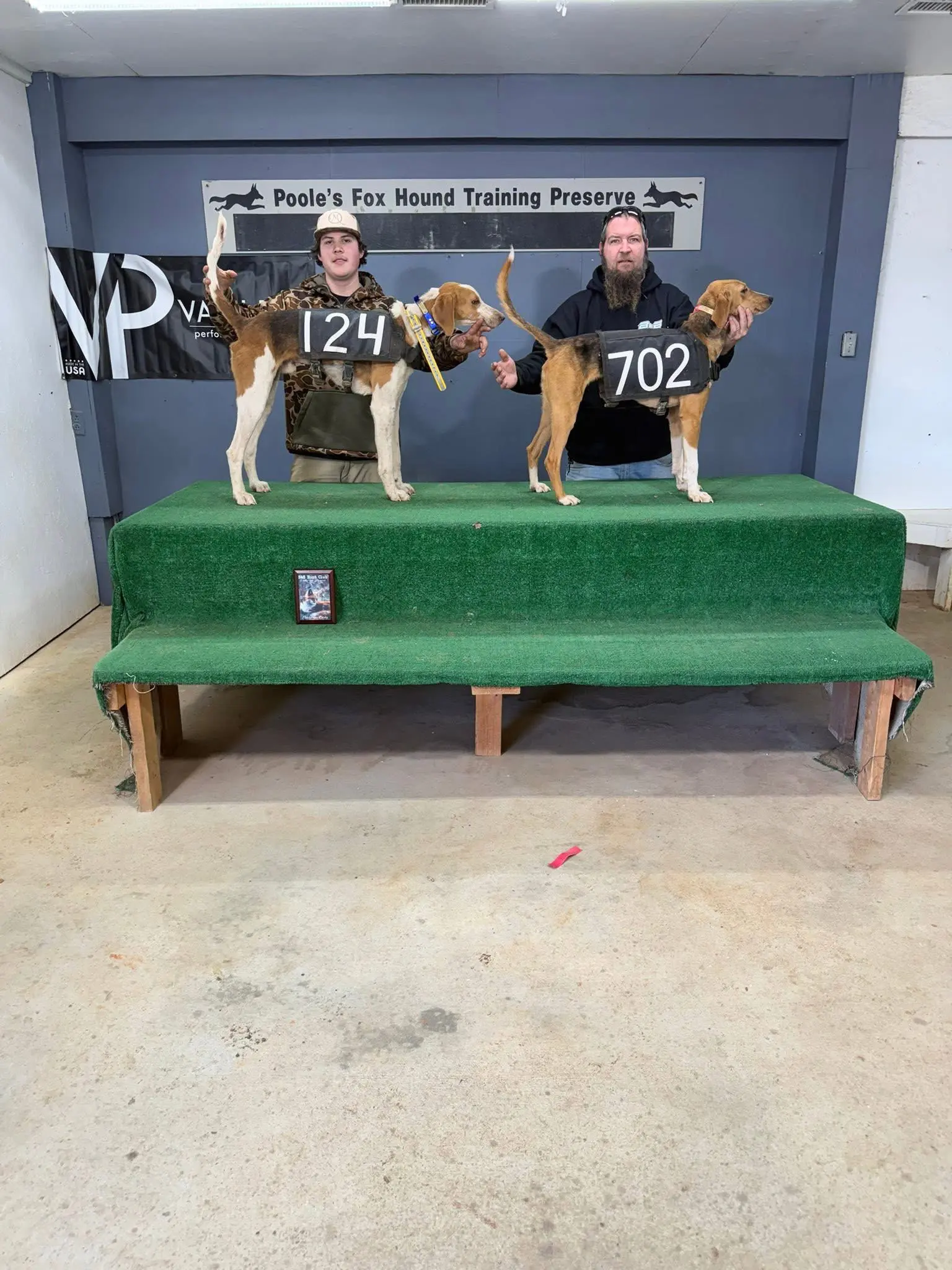 Two people with numbered dogs on platform.
