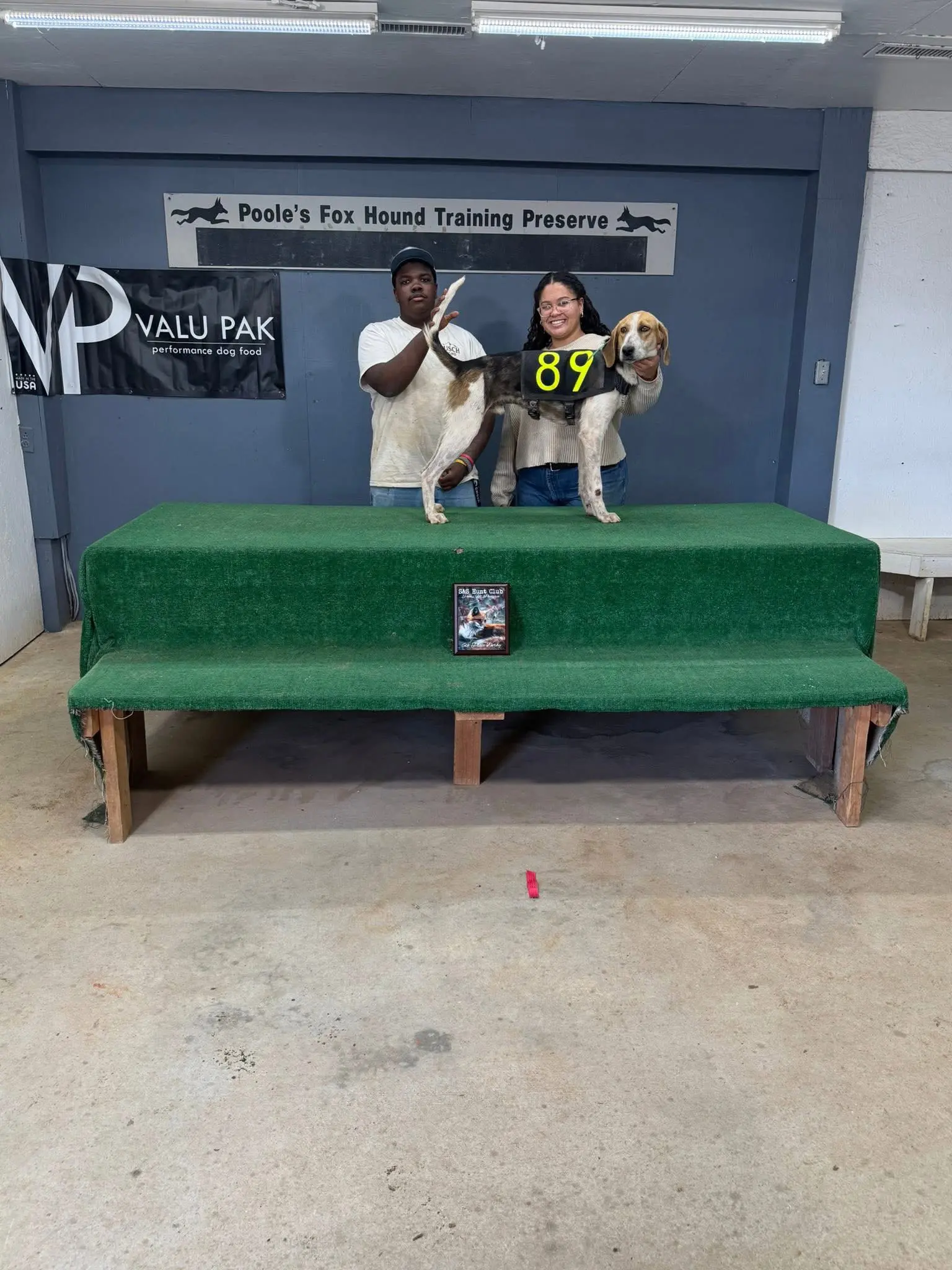 Dog show winners with hound on podium.