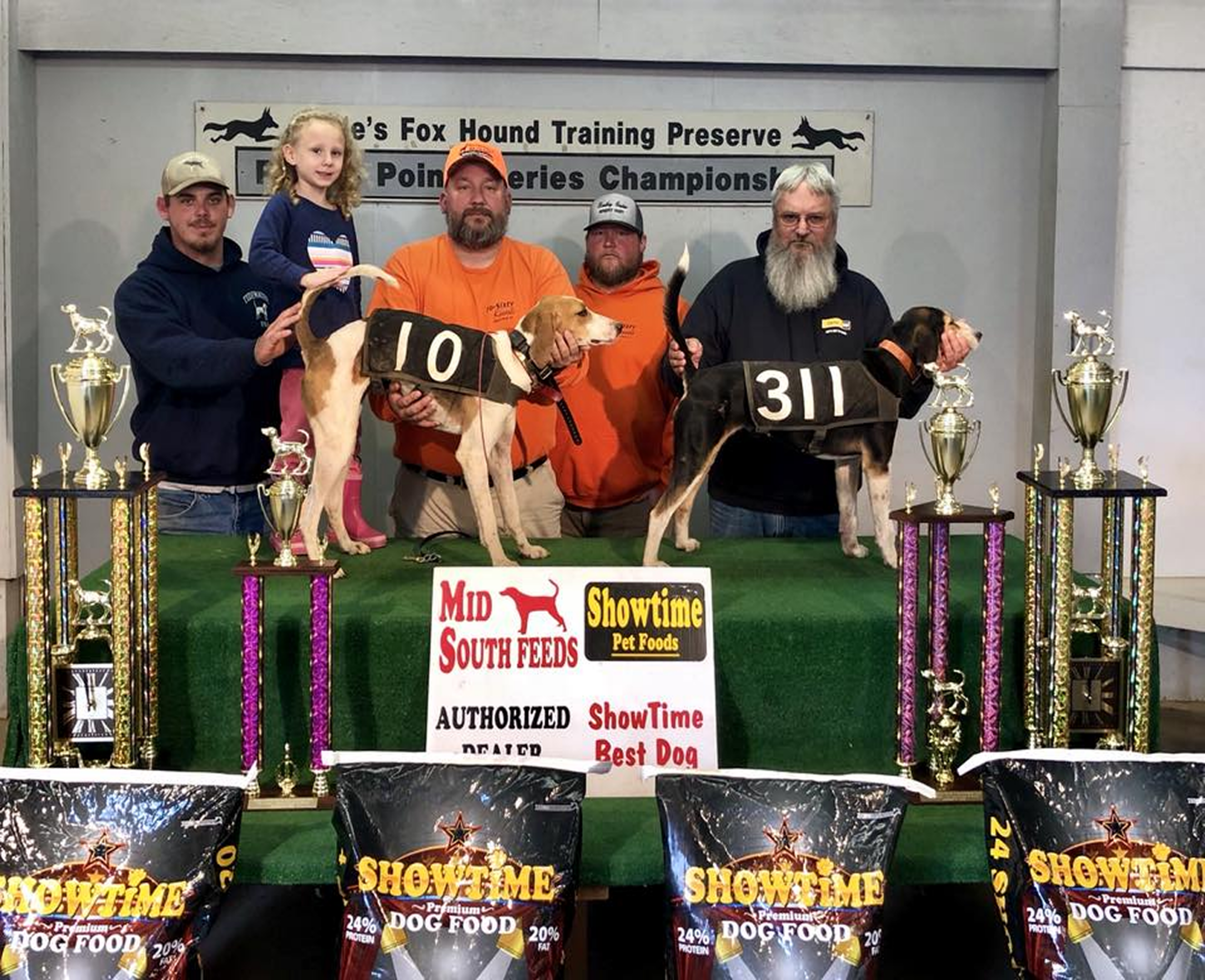 Men, girl, and dogs with trophies and banners.