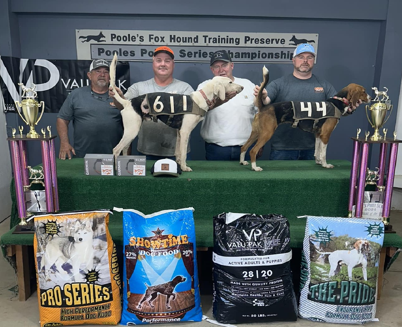 Three dogs standing on podiums at a dog event with prizes.